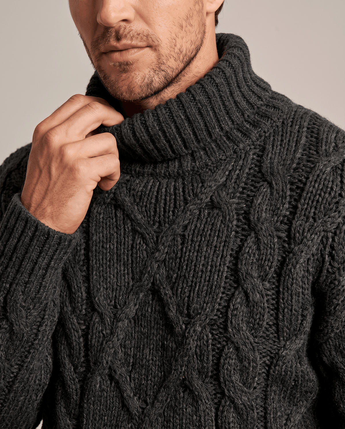 Close-up of man adjusting charcoal black fold-over turtleneck collar on chunky knit
