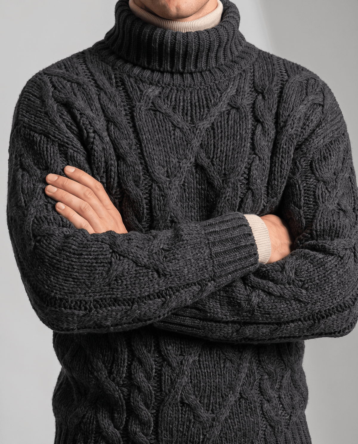 Charcoal black cable sweater worn with arms crossed showing sleeve cables and cuffs