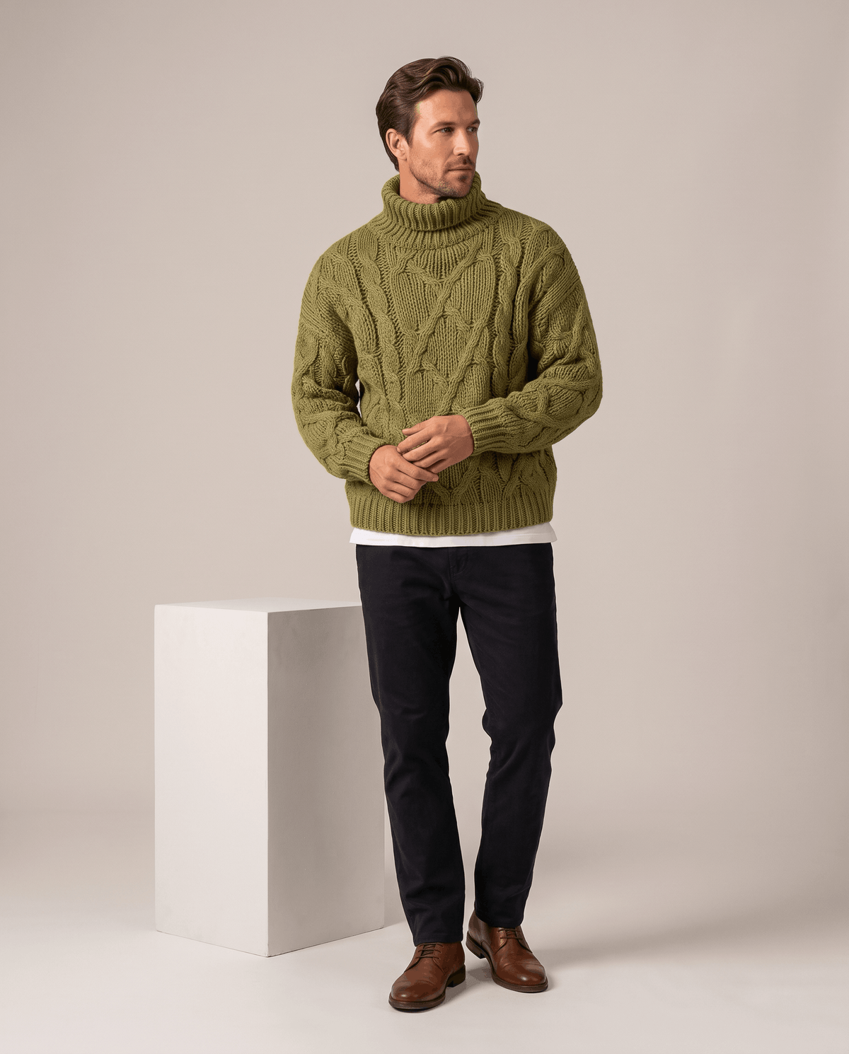 Model in olive green turtleneck layered over white tee with black trousers and brown boots