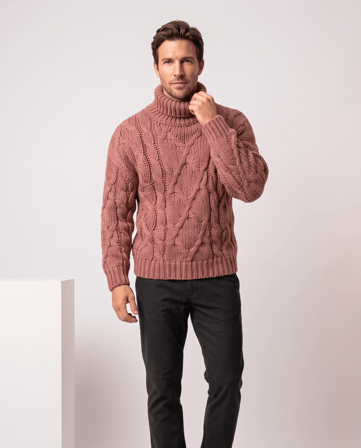 Model in dusty pink turtleneck sweater touching collar, paired with black trousers