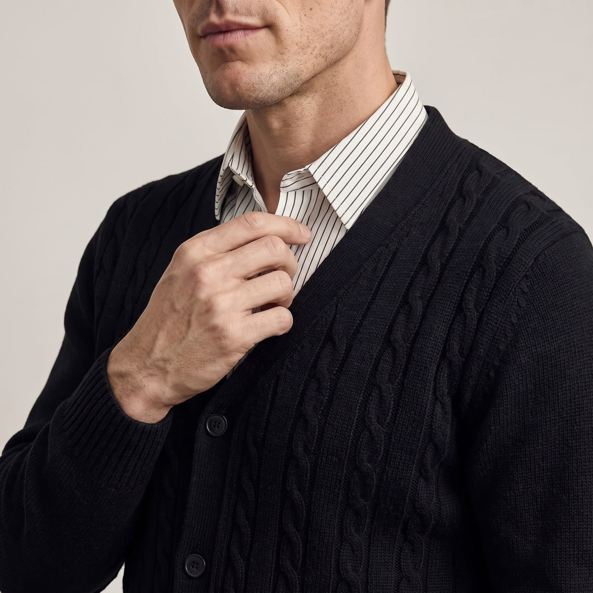 Hand at the V-neck of a black cardigan over a striped collared shirt