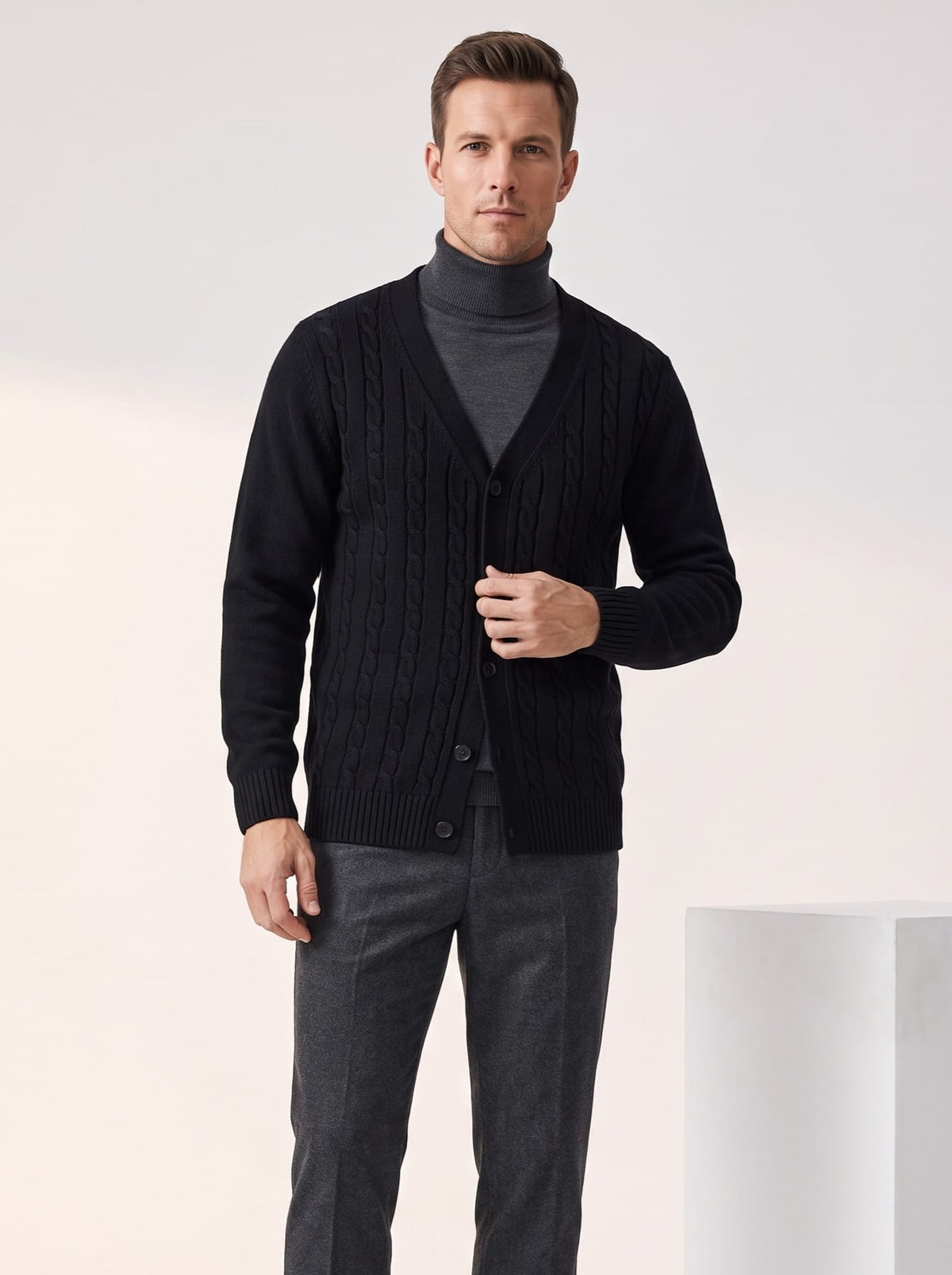 Black cable knit cardigan worn over a gray turtleneck with charcoal trousers