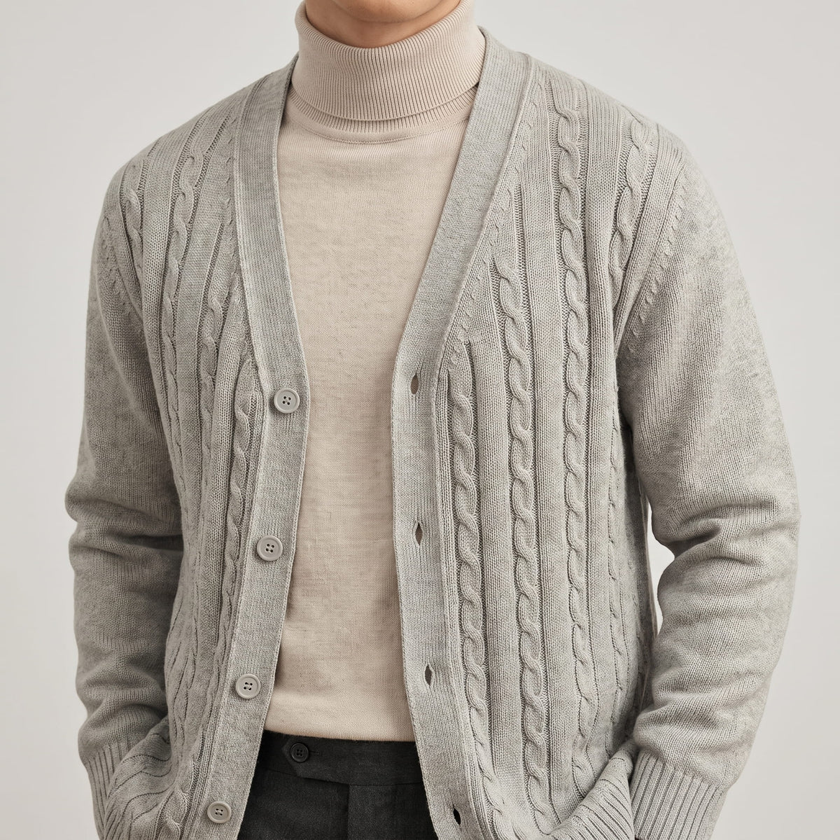 Close-up of the gray cable knit cardigan buttoned over a cream turtleneck