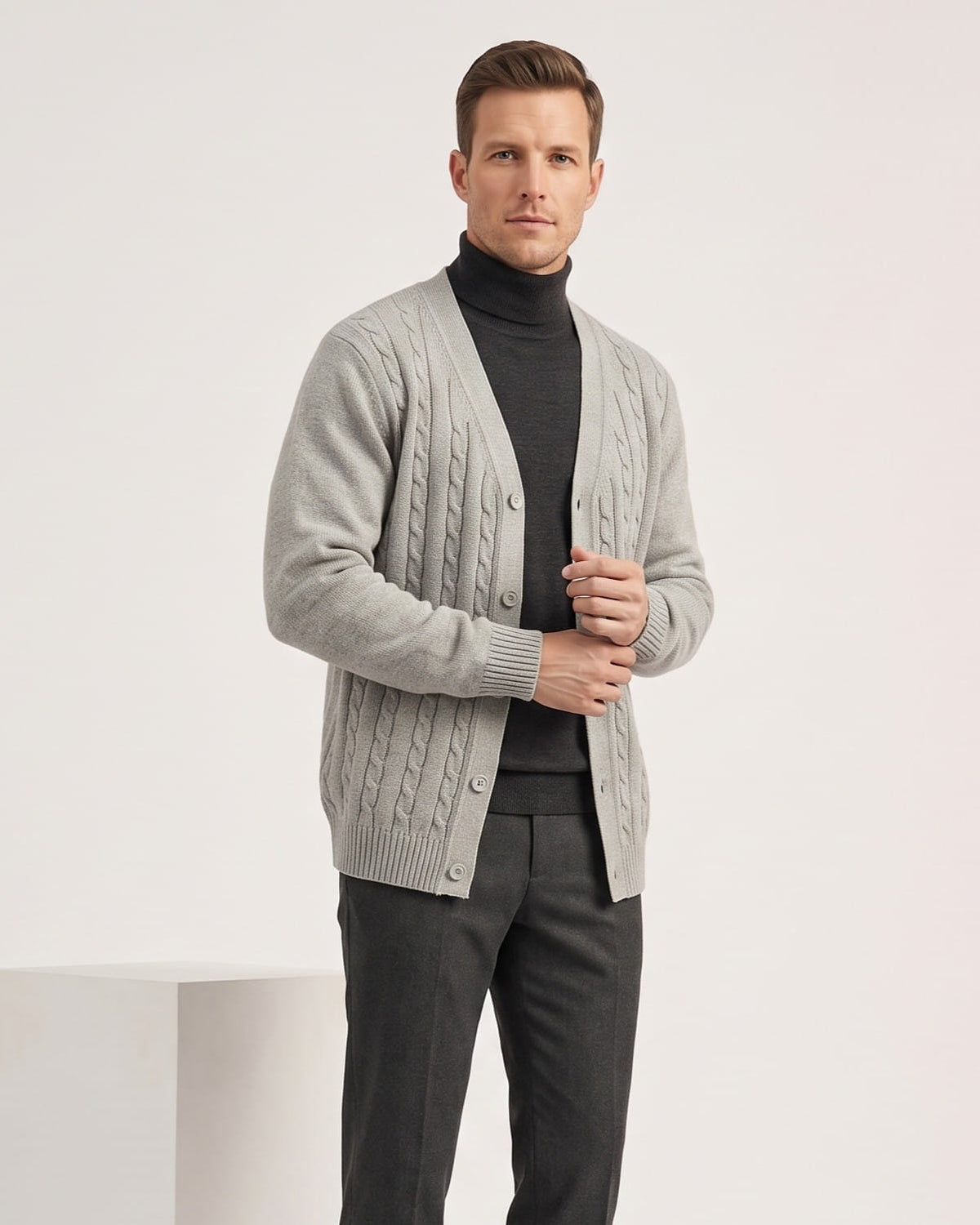 Man wearing a gray cable knit V-neck cardigan sweater over a black turtleneck