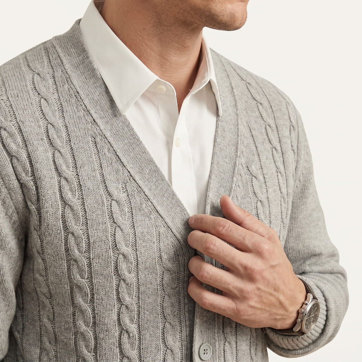 Hand at the button placket of a gray cardigan worn over a white shirt