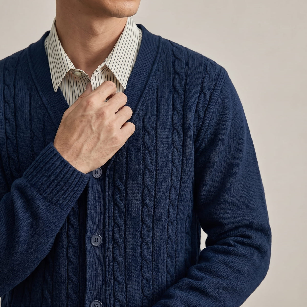 Hand at the V-neck of a navy cardigan over a striped collared shirt