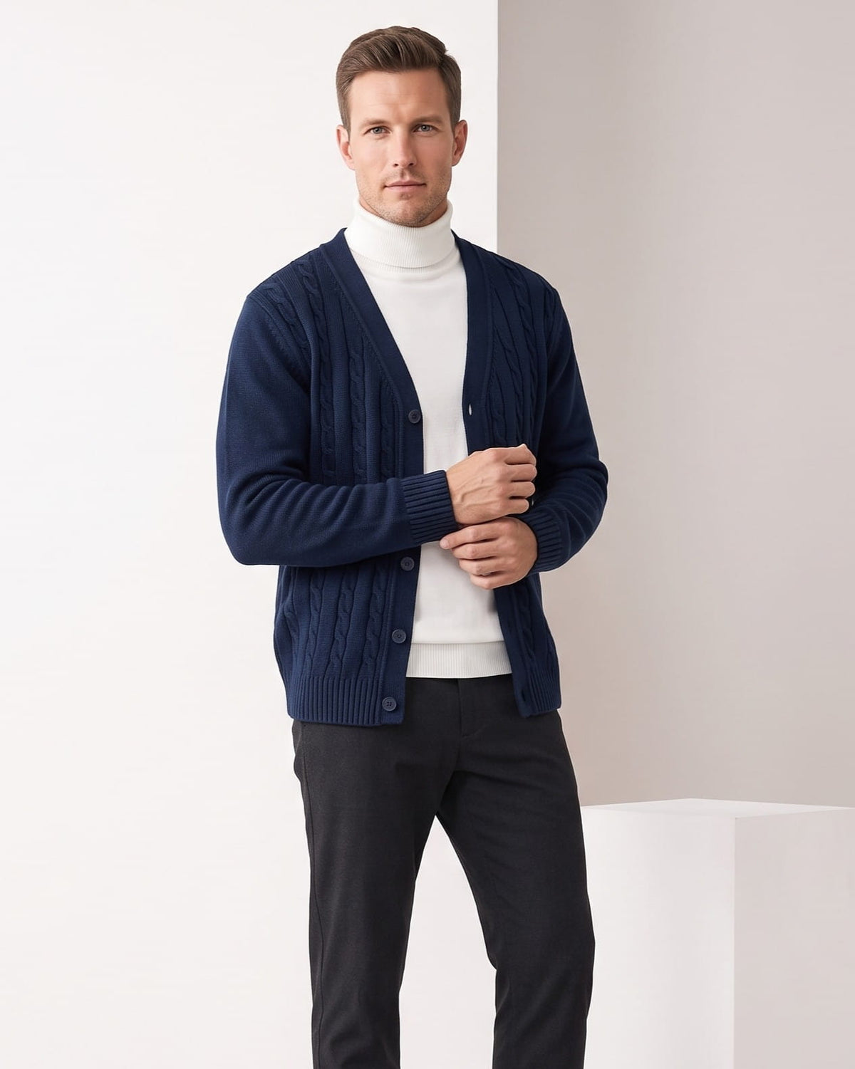 Navy cable knit V-neck cardigan over a white turtleneck with black trousers