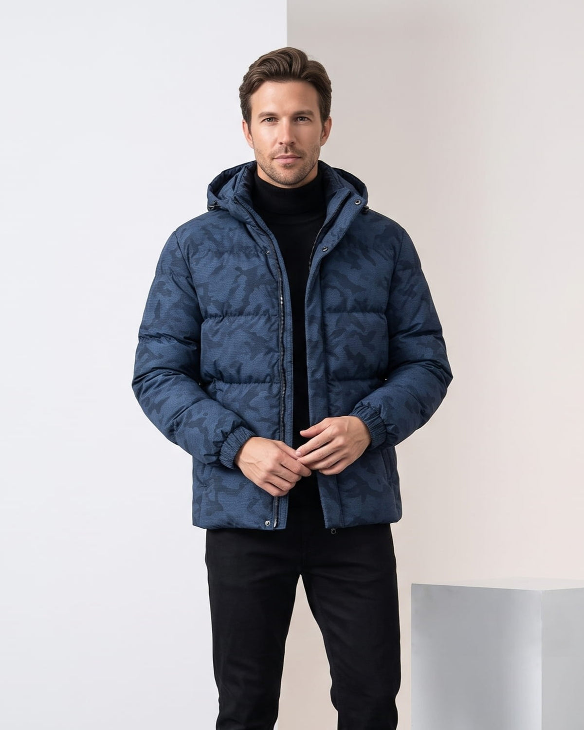 Man wearing navy camo-print hooded puffer jacket, worn open over a turtleneck