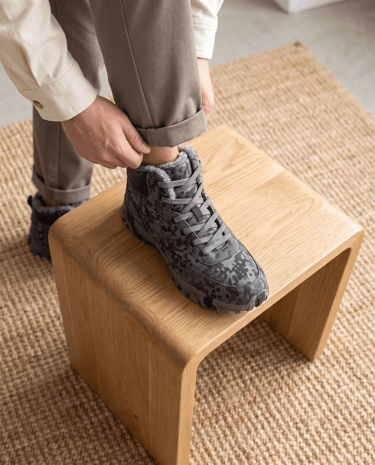 Hands lacing a dark camo boot propped on a pale wooden bench
