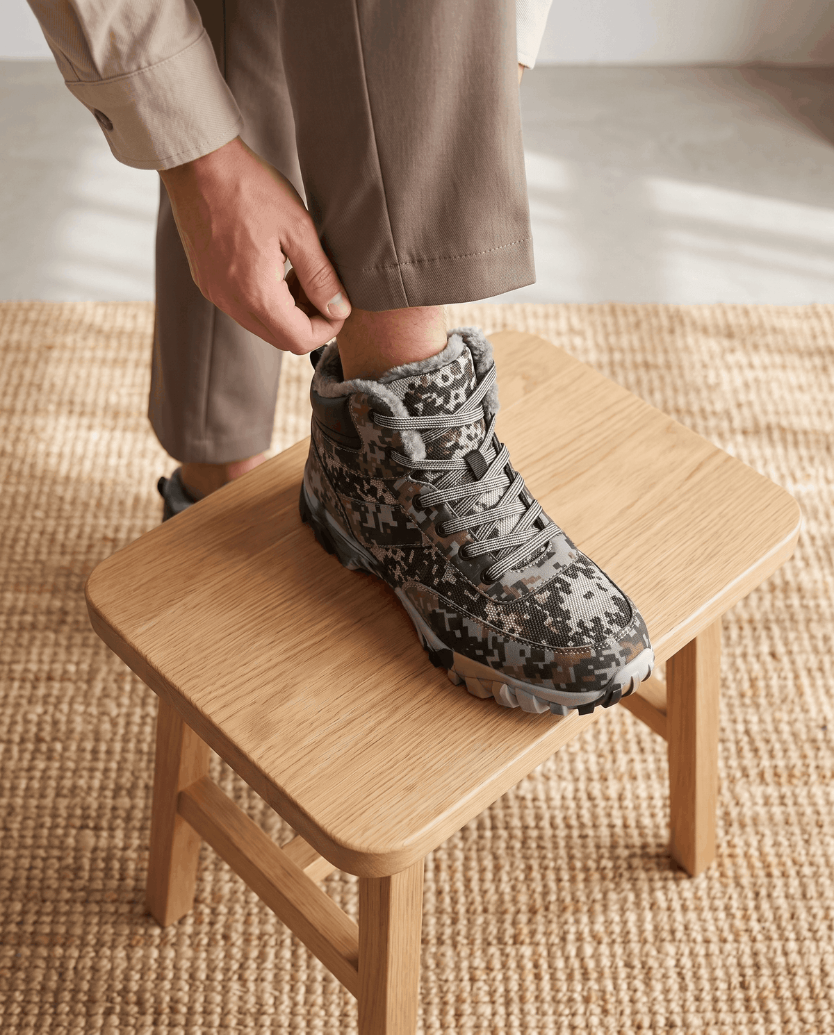 Hand pulling the laces of a green camo boot resting on a wooden bench