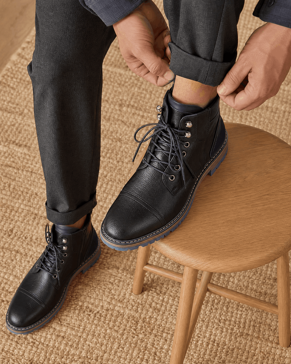 Black smooth grain leather cap toe boots with lace-up front, side zip, and rugged lug outsole worn with cuffed trousers.