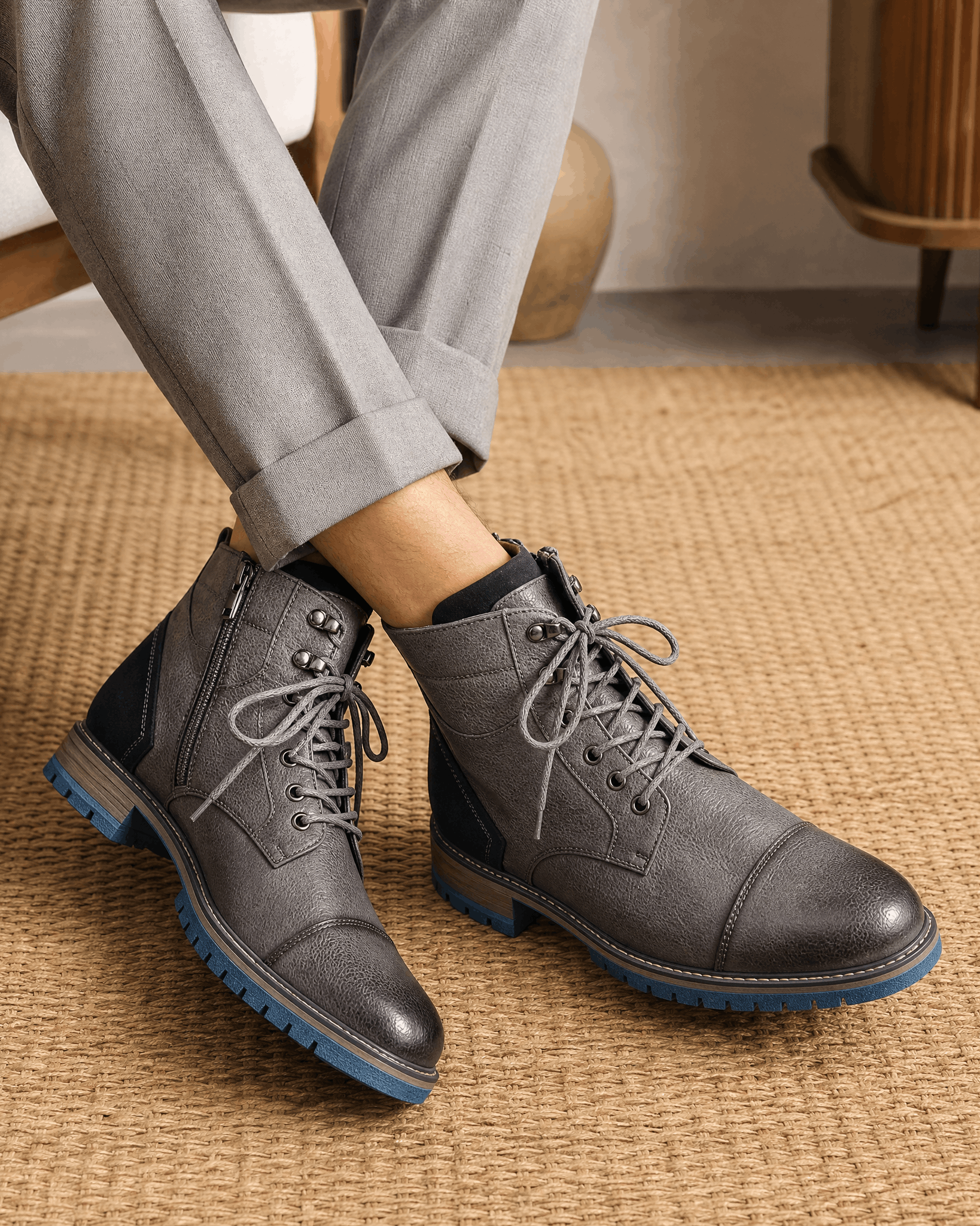 Gray smooth grain leather cap toe boots with side zips, lace-up fronts, and blue lug rubber outsoles worn with grey trousers.