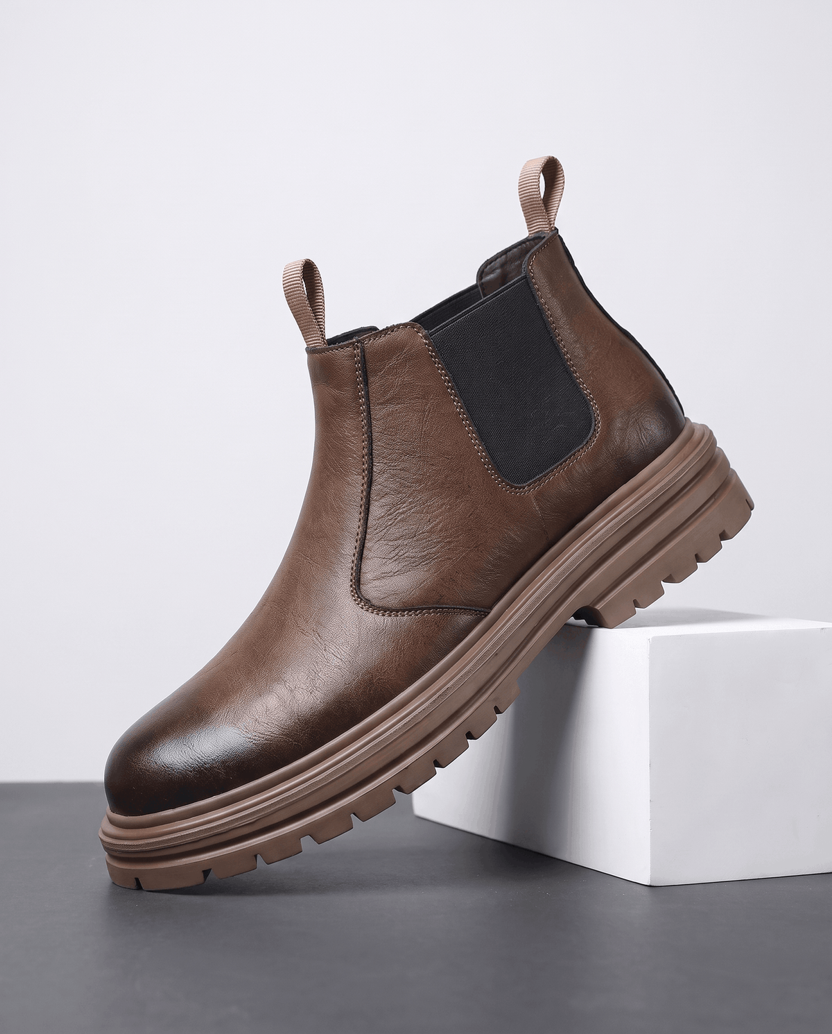 Brown pebbled leather Chelsea boots with black elastic side panels, twin pull tabs, and a chunky lugged platform sole.