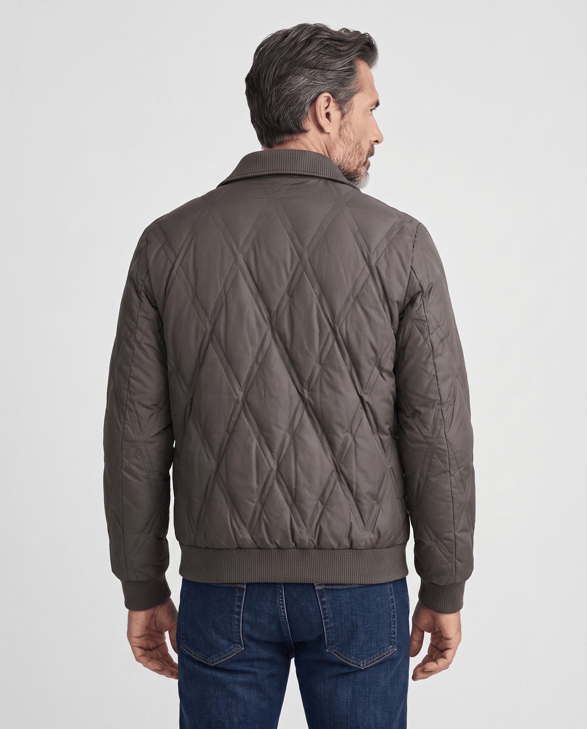 Back view of a man wearing a dark brown diamond quilted puffer jacket with ribbed hem
