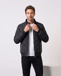 Man wearing black diamond-quilted bomber jacket with stand collar, holding the collar
