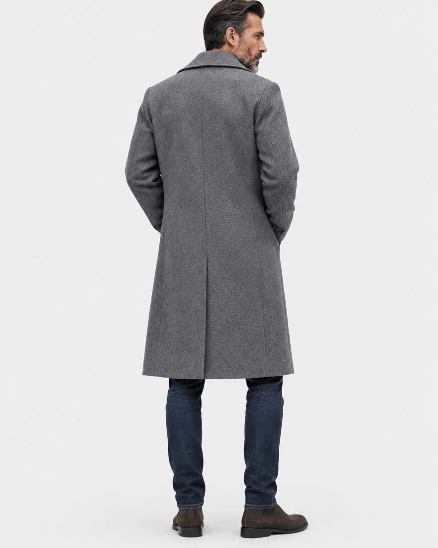 Back of the dark gray long overcoat showing a smooth back and straight hem over dark jeans