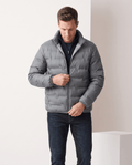 Man wearing gray duck down puffer jacket with stand collar, adjusting the front zip