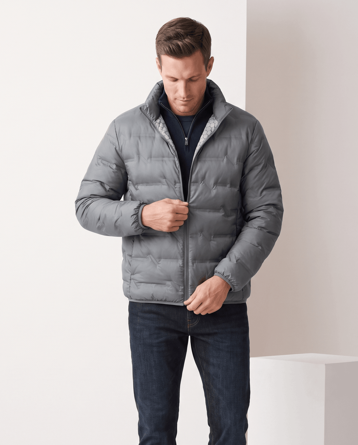 Man wearing gray duck down puffer jacket with stand collar, adjusting the front zip