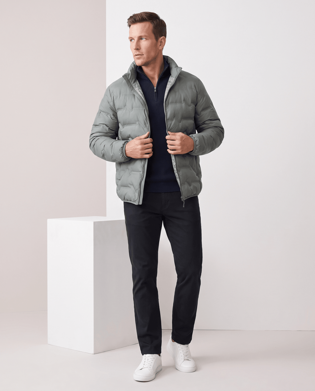 Gray jacket over a navy sweater with black trousers and white sneakers