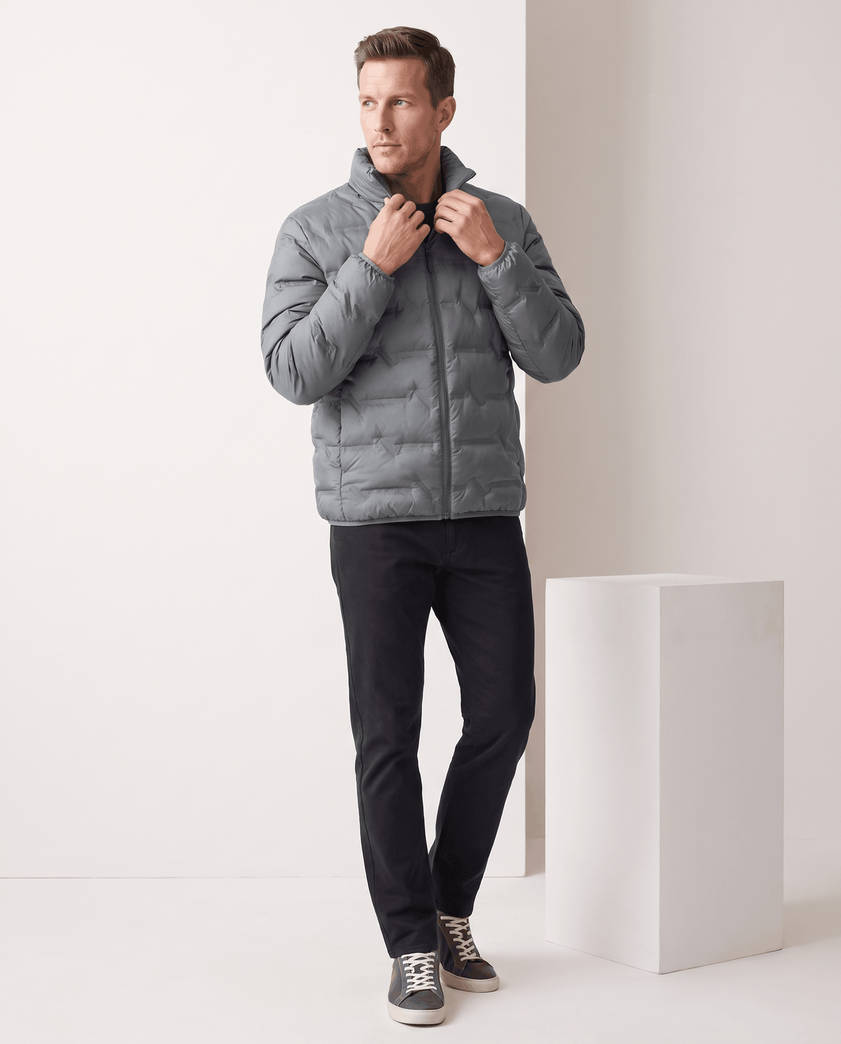 Gray jacket being zipped at the collar, full-length view with dark trousers