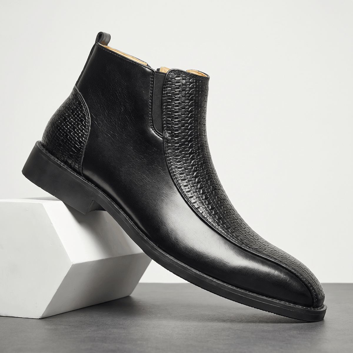 Black leather ankle boot with basketweave embossed panels, side zip, and a softly squared toe on a low stacked heel.