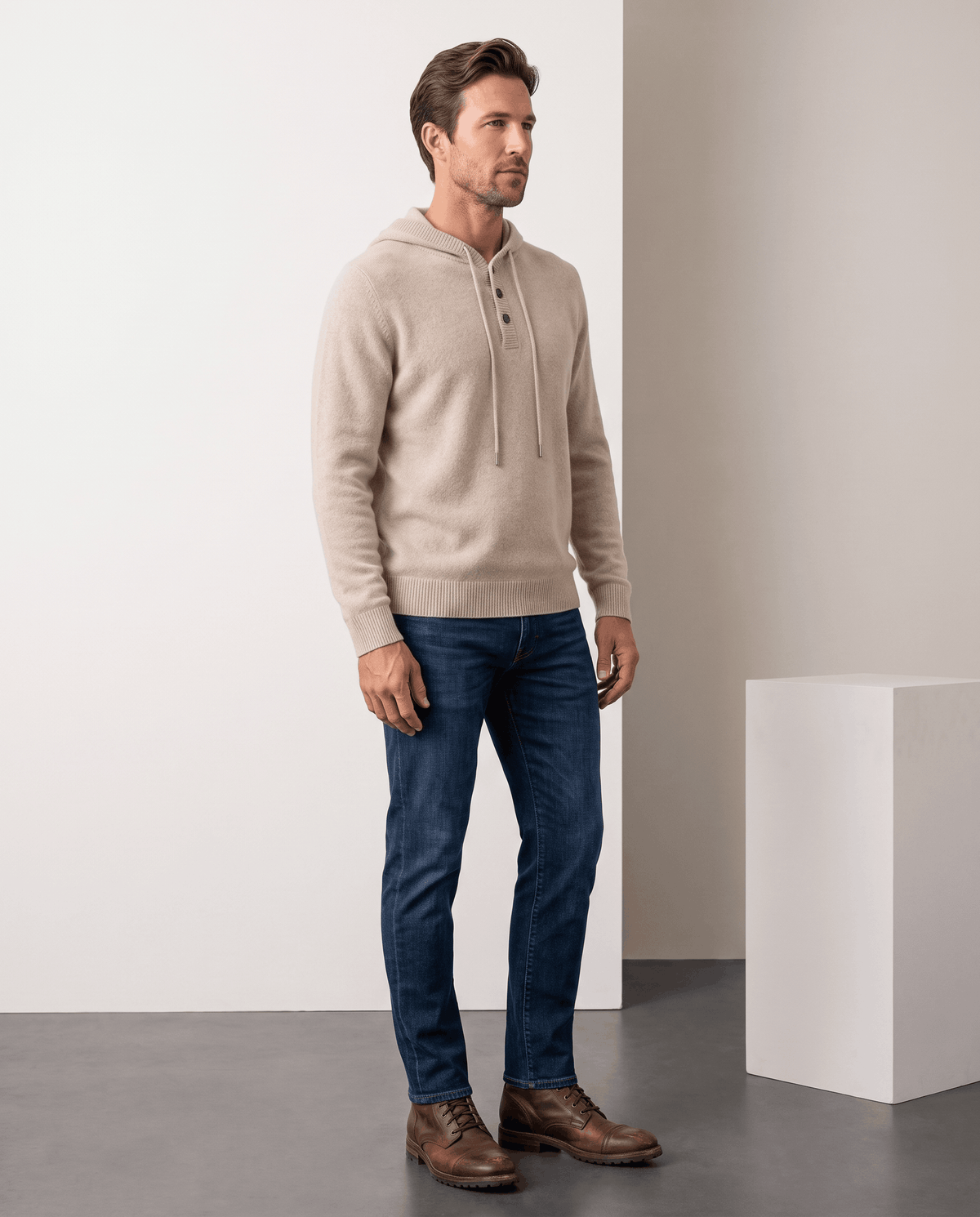 Full-length view of a man in a beige knit hoodie, dark jeans and brown boots