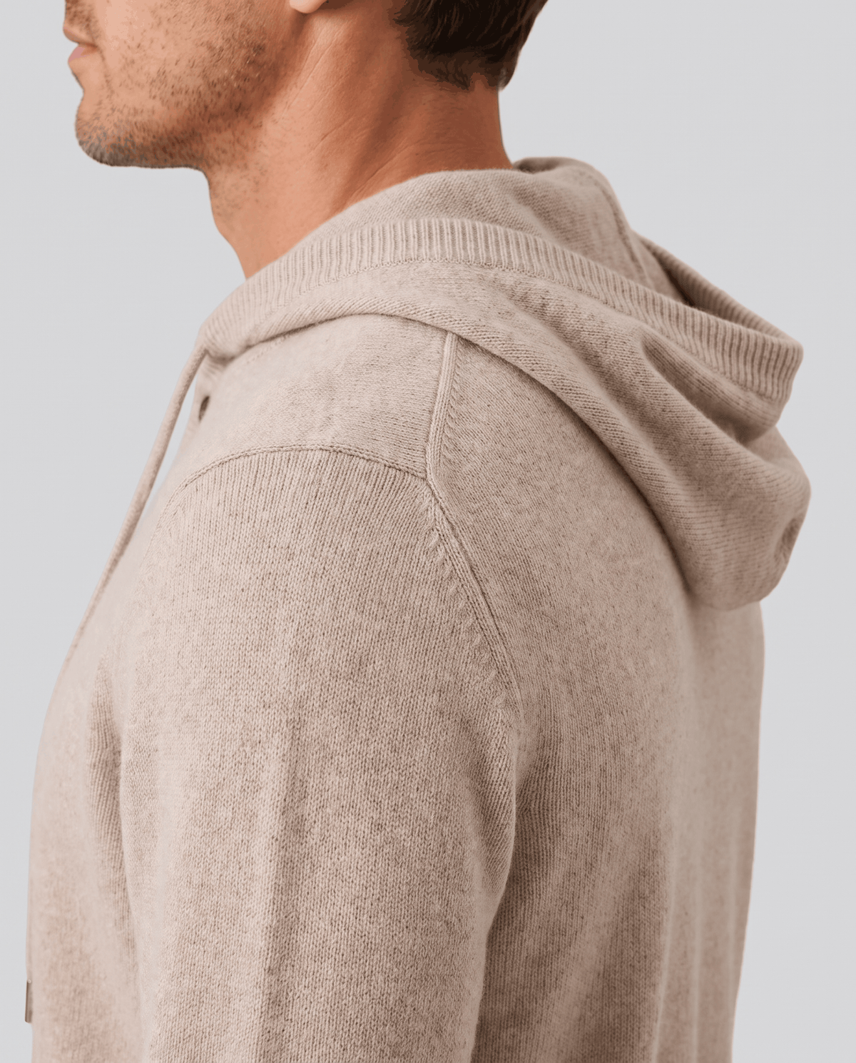 Side profile of a beige knit hoodie showing the hood and shoulder seam