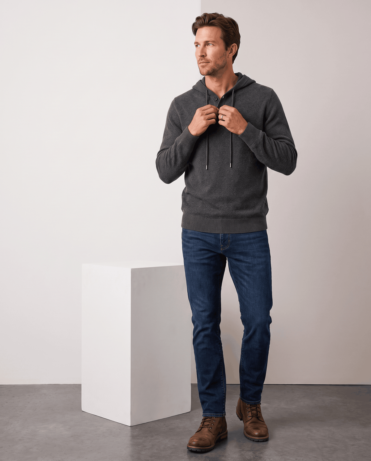 Full-length view of a man in a dark gray knit hoodie, blue jeans and boots