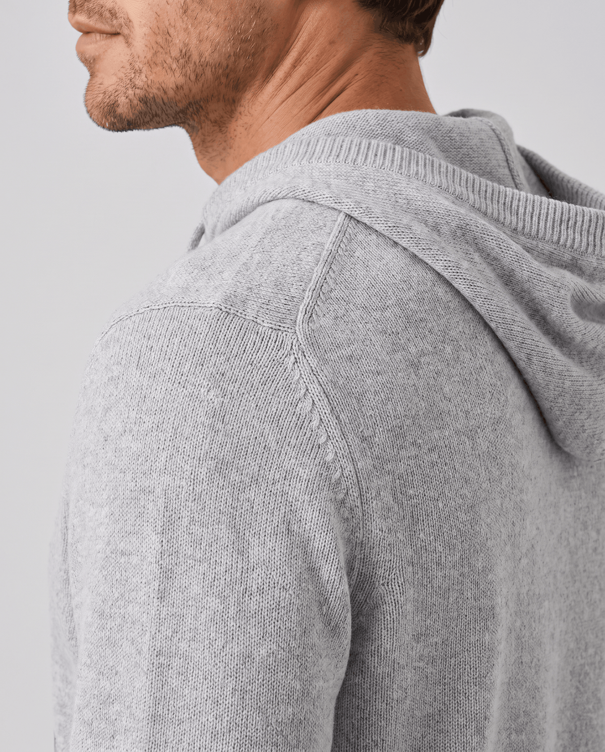 Side profile of a light gray knit hoodie showing the hood and shoulder