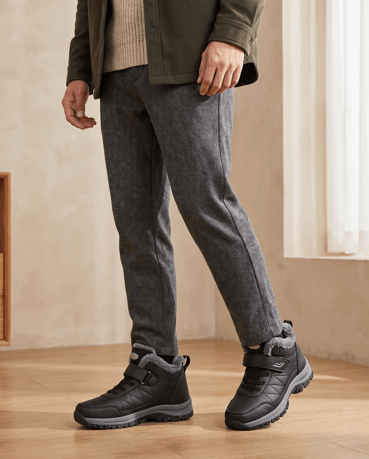 Person wearing black winter boots with gray trousers in a minimalist indoor setting.