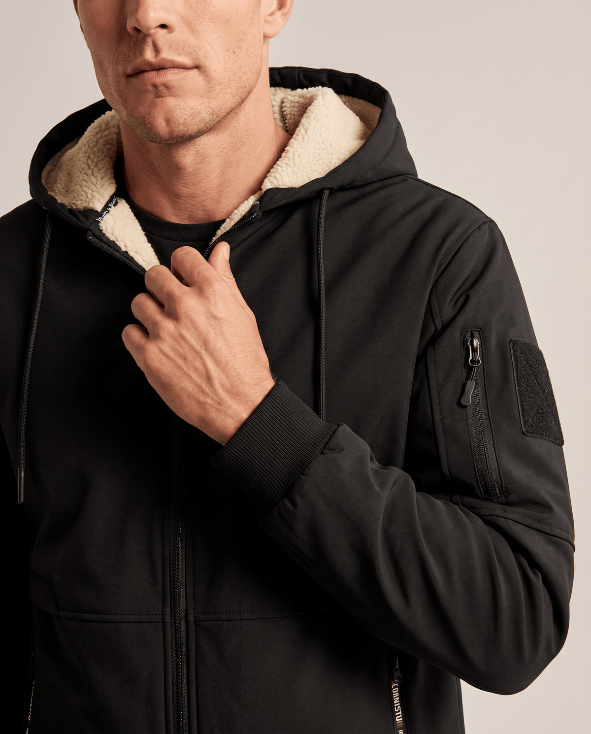 Close-up of black jacket collar, zip and fleece-lined hood with a hand on the drawstring