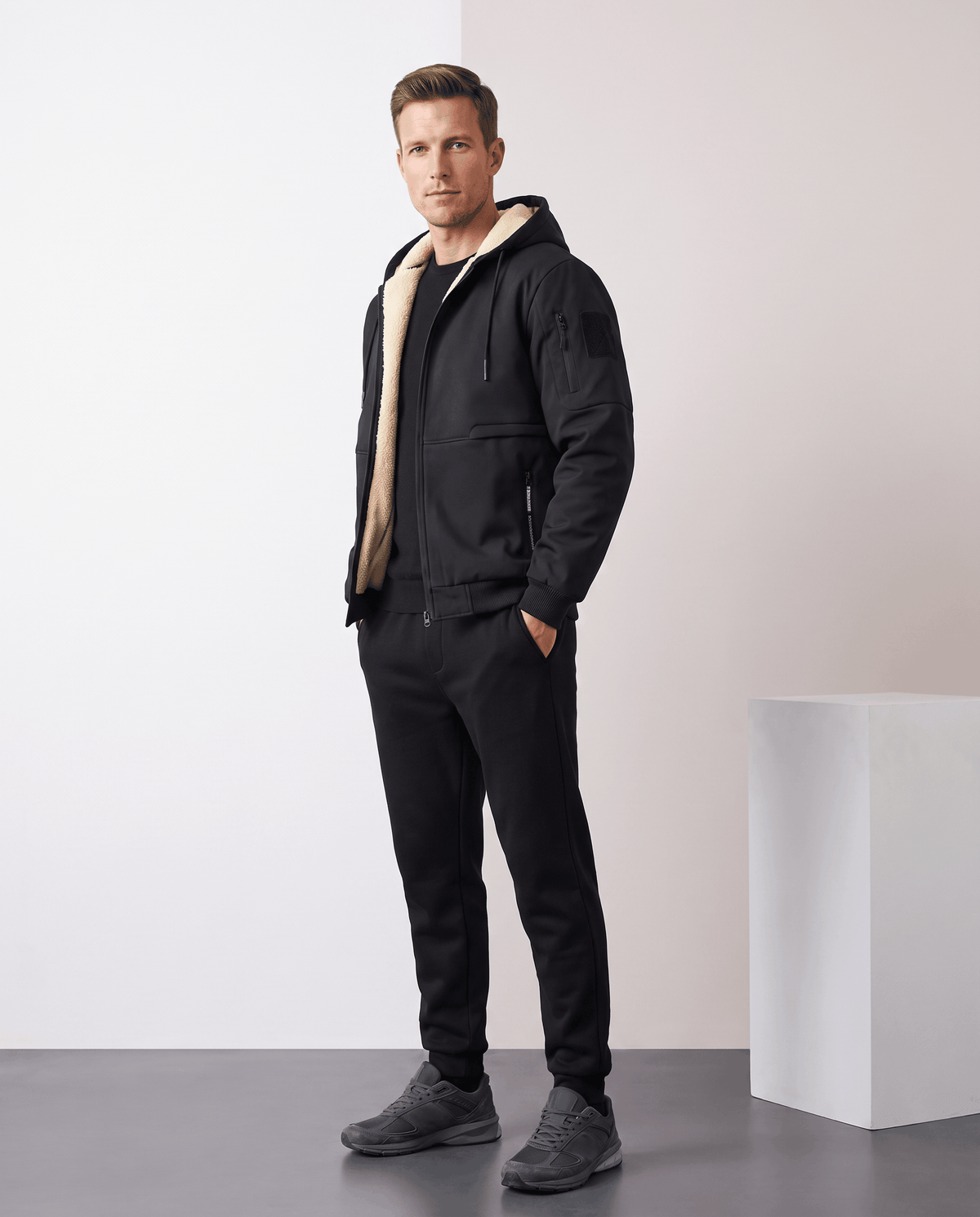 Full-length view of black hooded jacket styled with black pants and dark sneakers