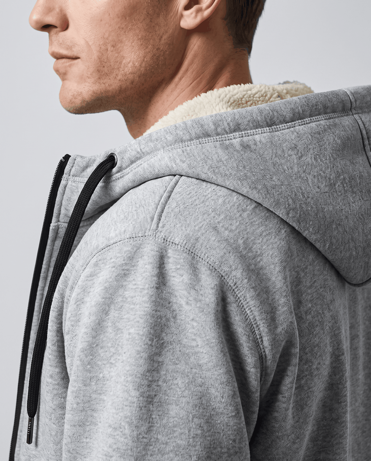 Side close-up of gray jacket hood with drawstring and soft fleece lining at the collar