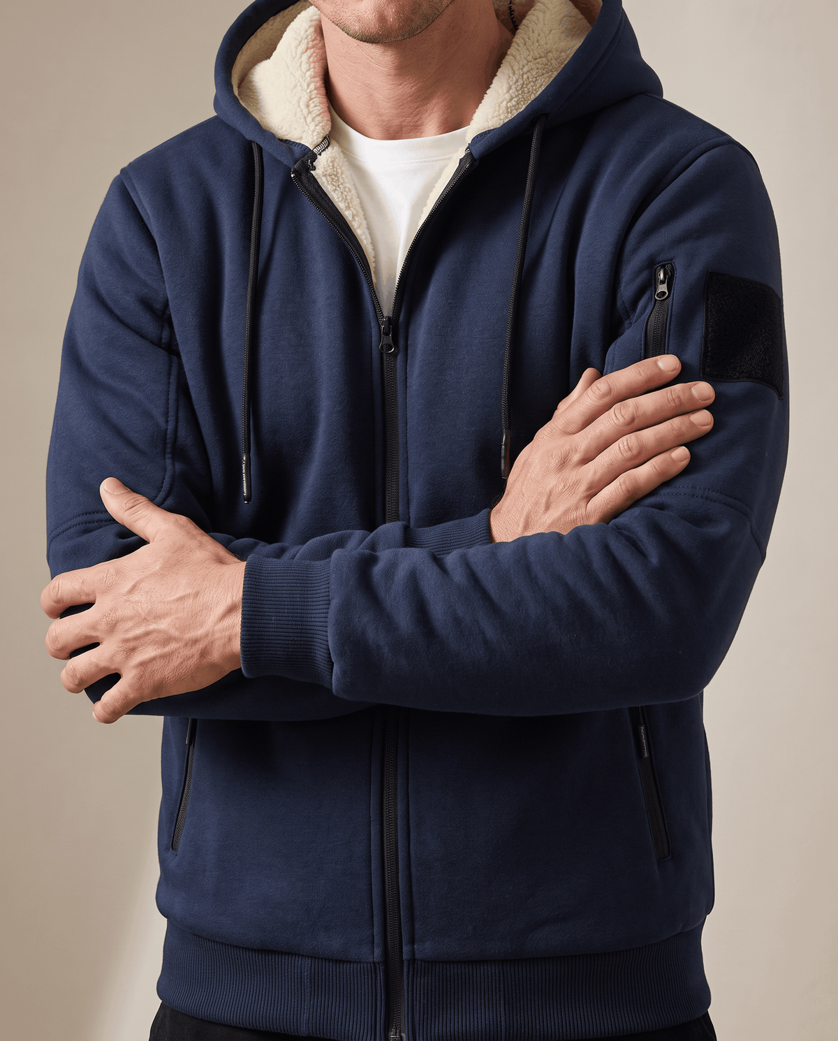 Navy blue jacket zipped up with arms crossed, showing the fleece-lined hood and sleeve pocket