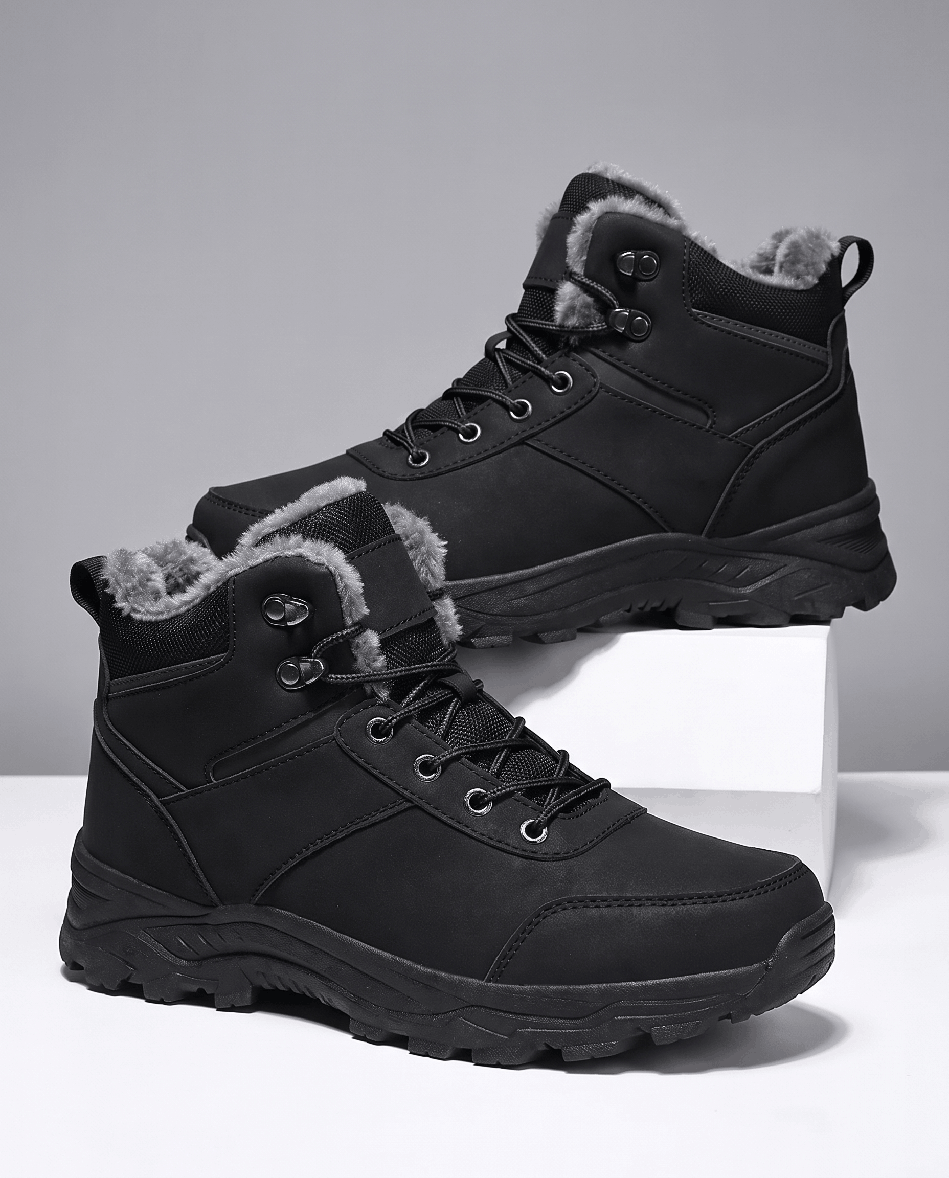 Black winter ankle boots with lace-up fronts, padded collars, and rugged lug soles displayed on white blocks.