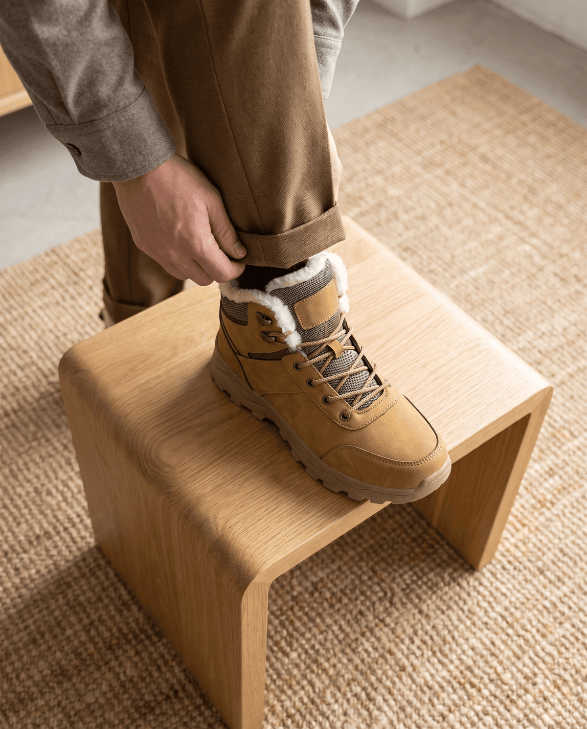 Person placing a gray winter boot on a wooden stool.