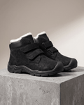 Black fleece-lined boots with twin hook-and-loop straps and a toe bumper, displayed on a concrete pedestal.
