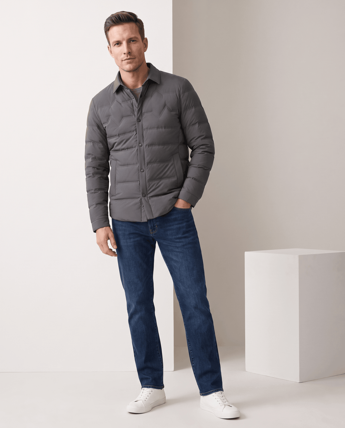 Man standing in a gray quilted puffer jacket with blue jeans, full-length view