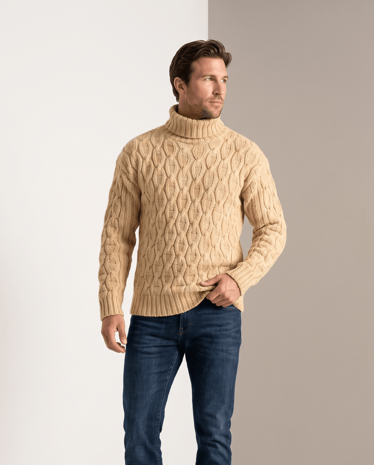Model in sand beige cable turtleneck with blue jeans beside white wall