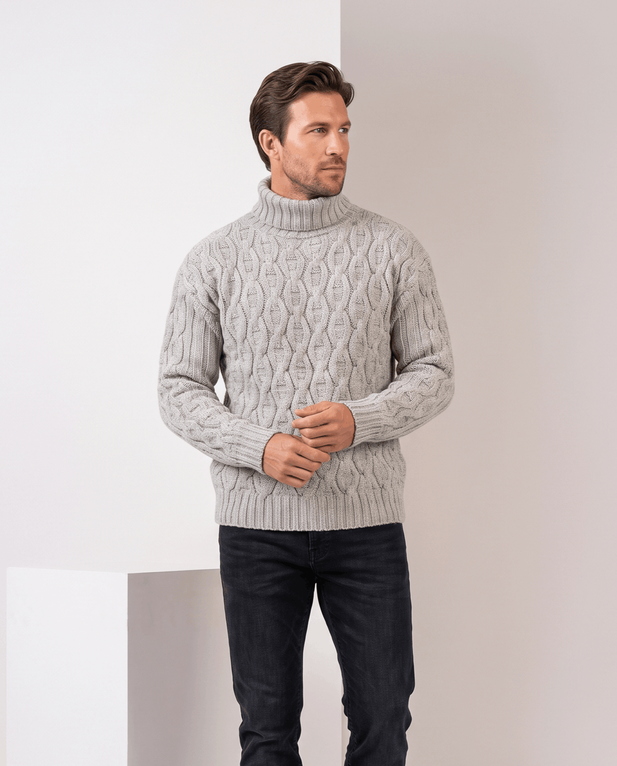 Model in light gray cable turtleneck with black jeans and hands clasped