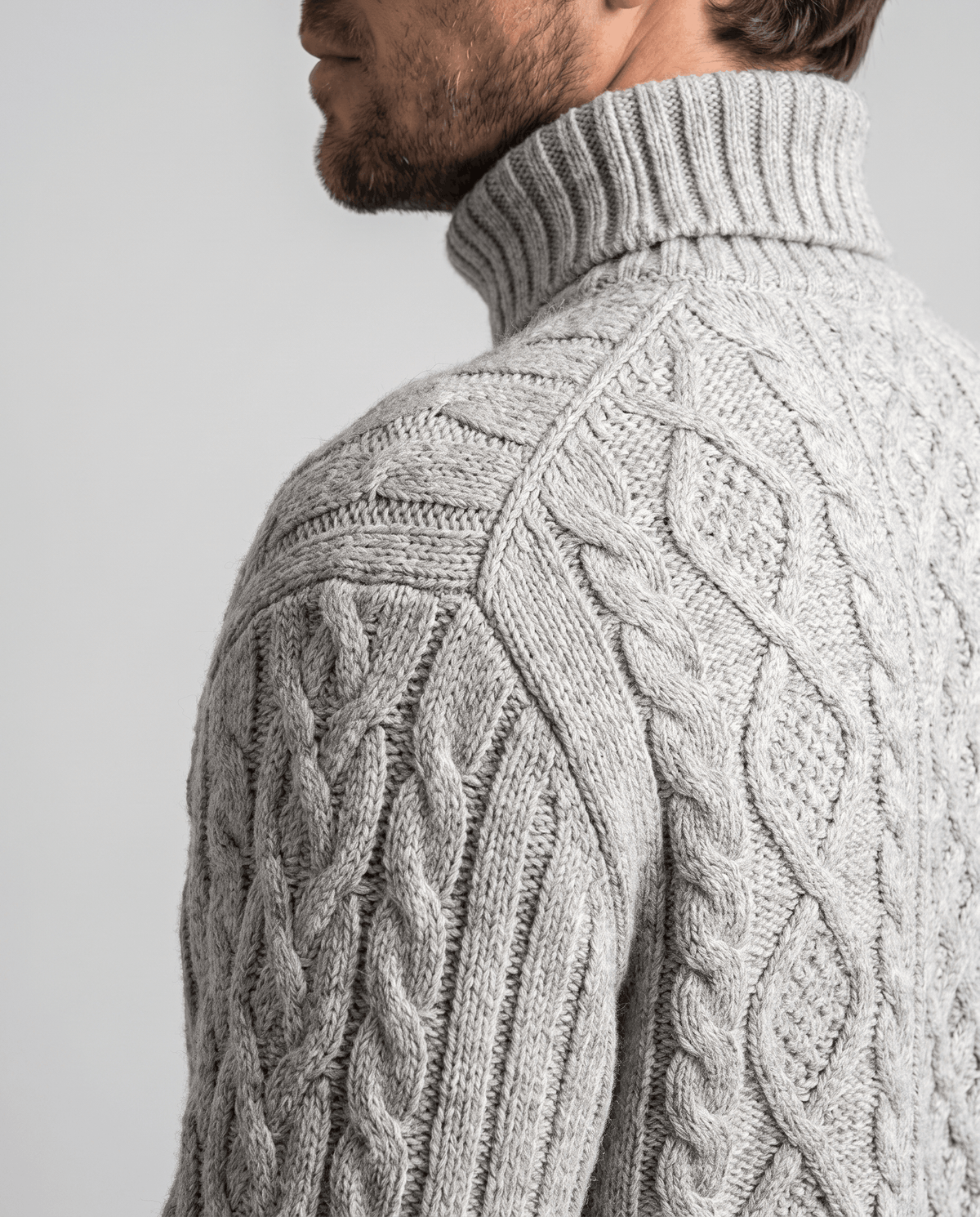 Shoulder close-up of light gray sweater showing linked oval cables and ribbed panel
