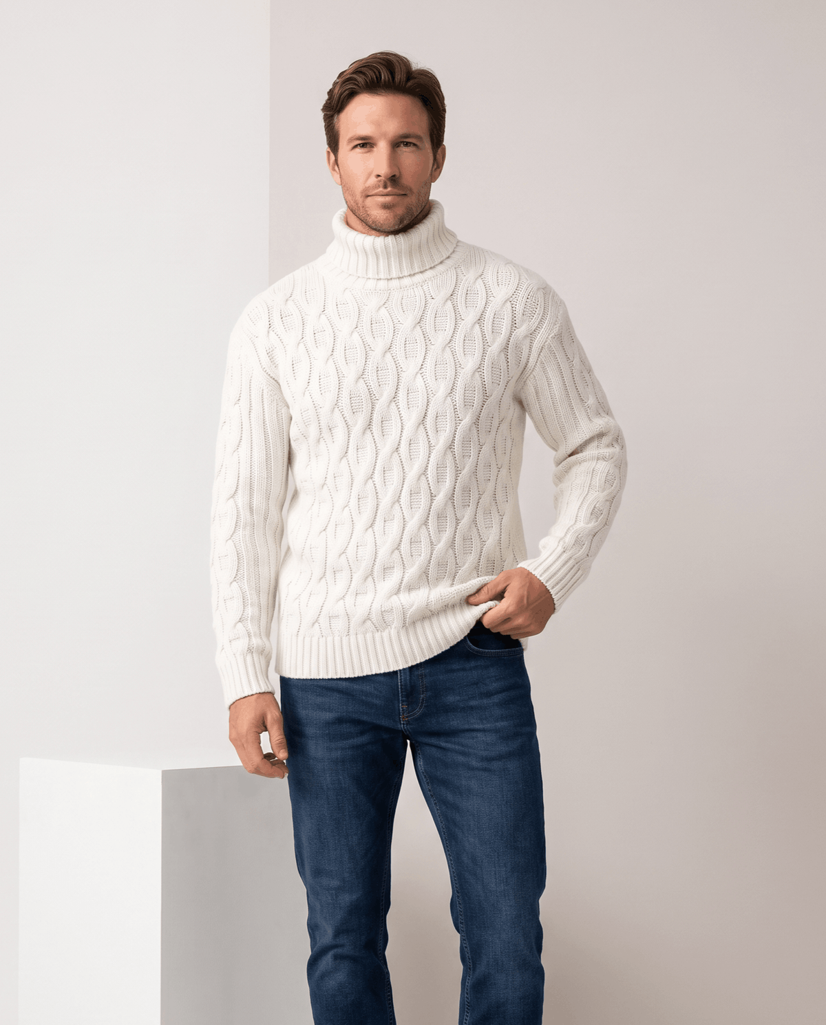 Man wearing men's honeycomb cable-knit turtleneck sweater in white with dark blue jeans