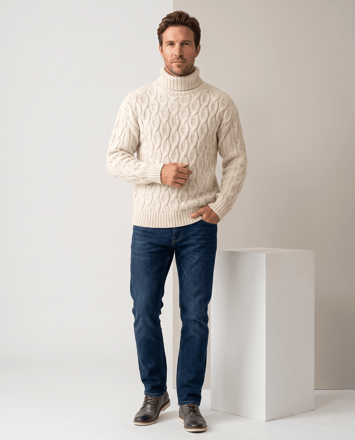 Model in white cable turtleneck with hand in jeans pocket beside a white plinth