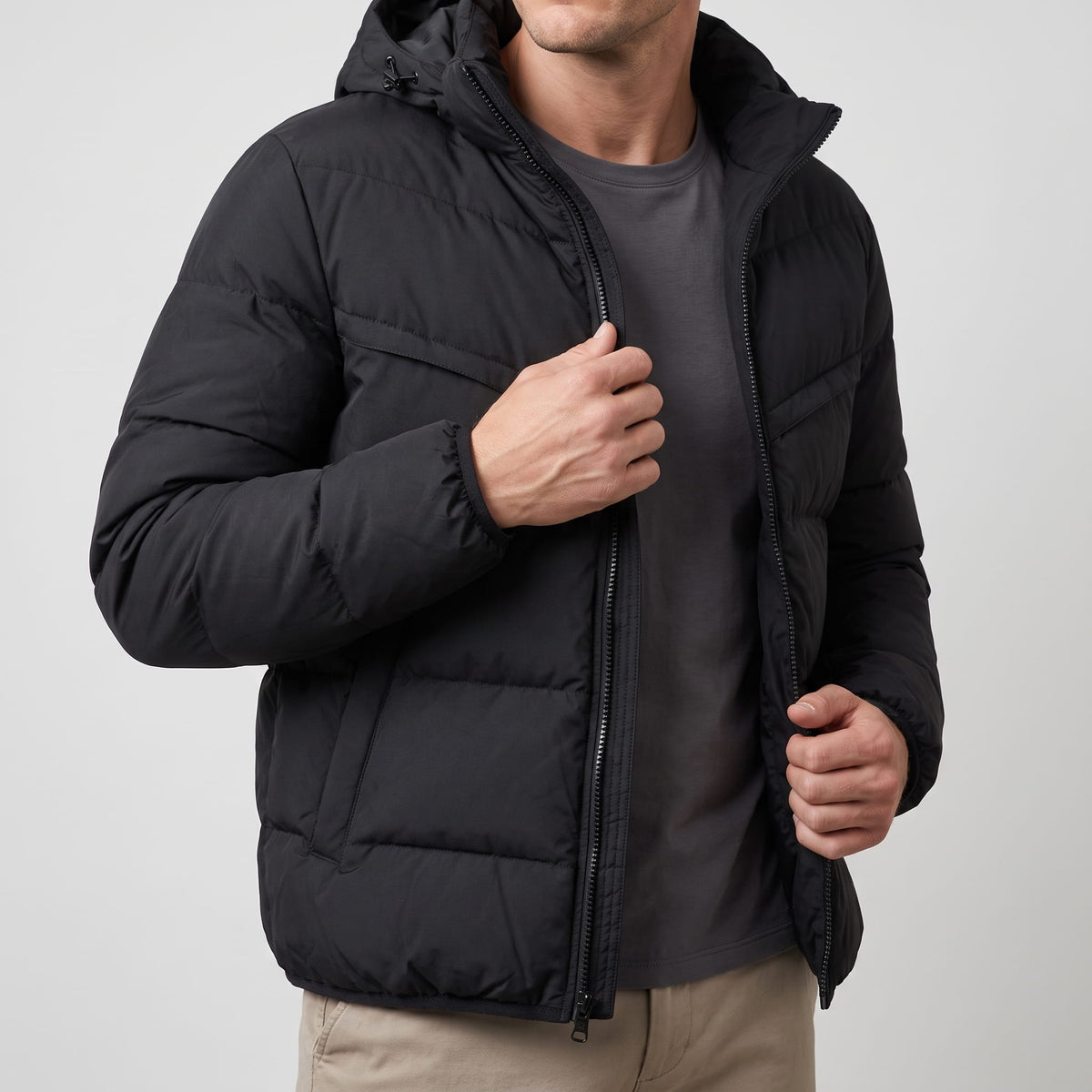 Black jacket worn open over a grey tee, hand holding the zip placket