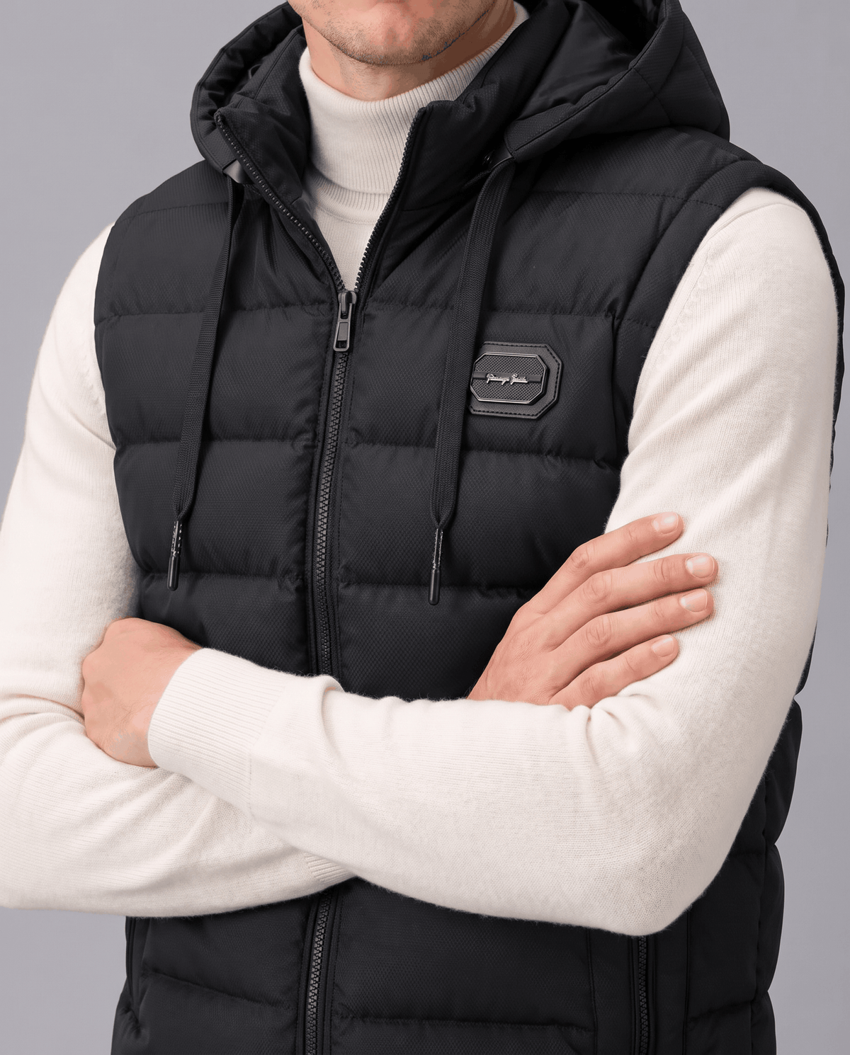 Close-up of black vest with chest badge and zip front, arms crossed over a white sweater