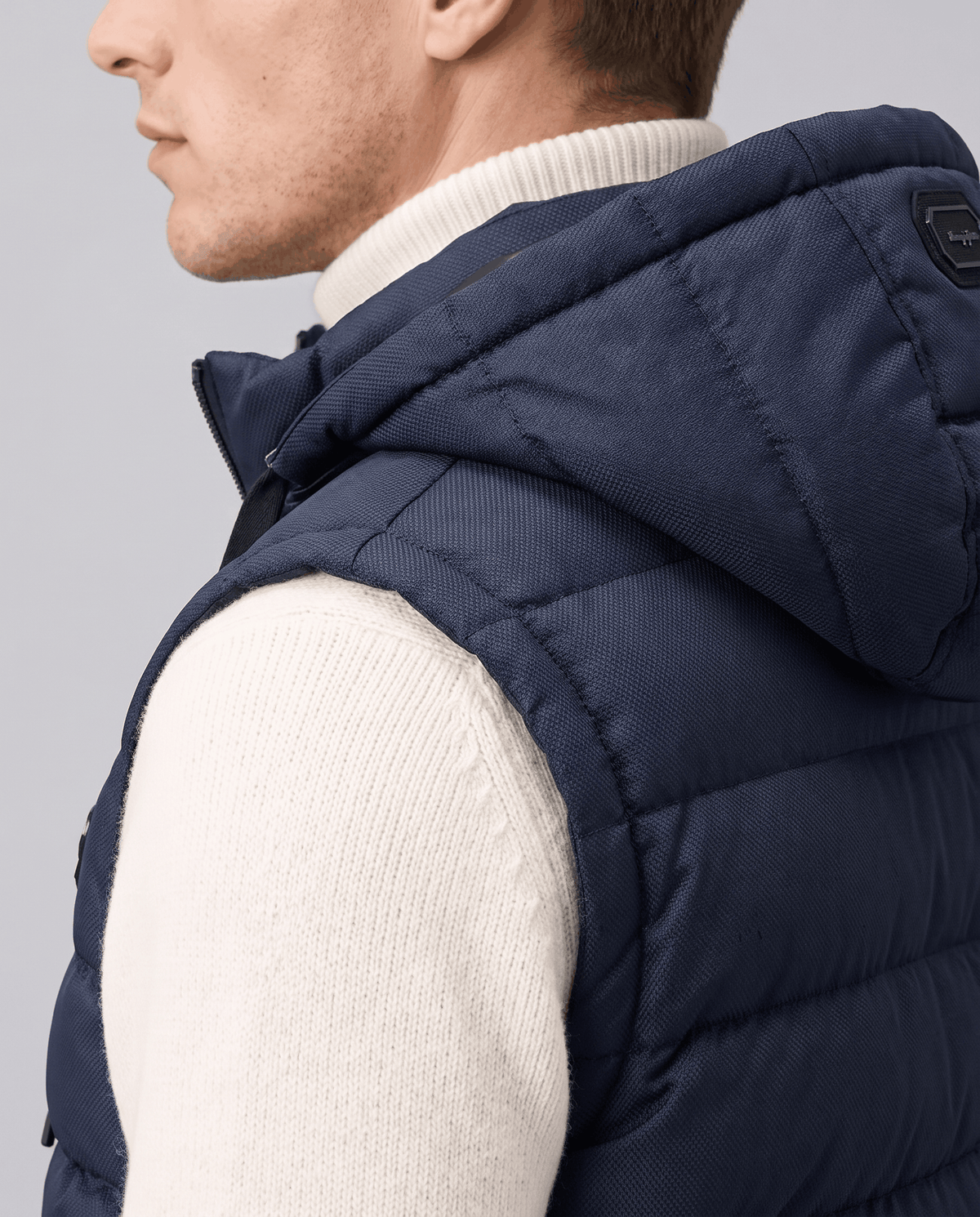 Side close-up of navy vest showing the hood and high collar over a cream sweater