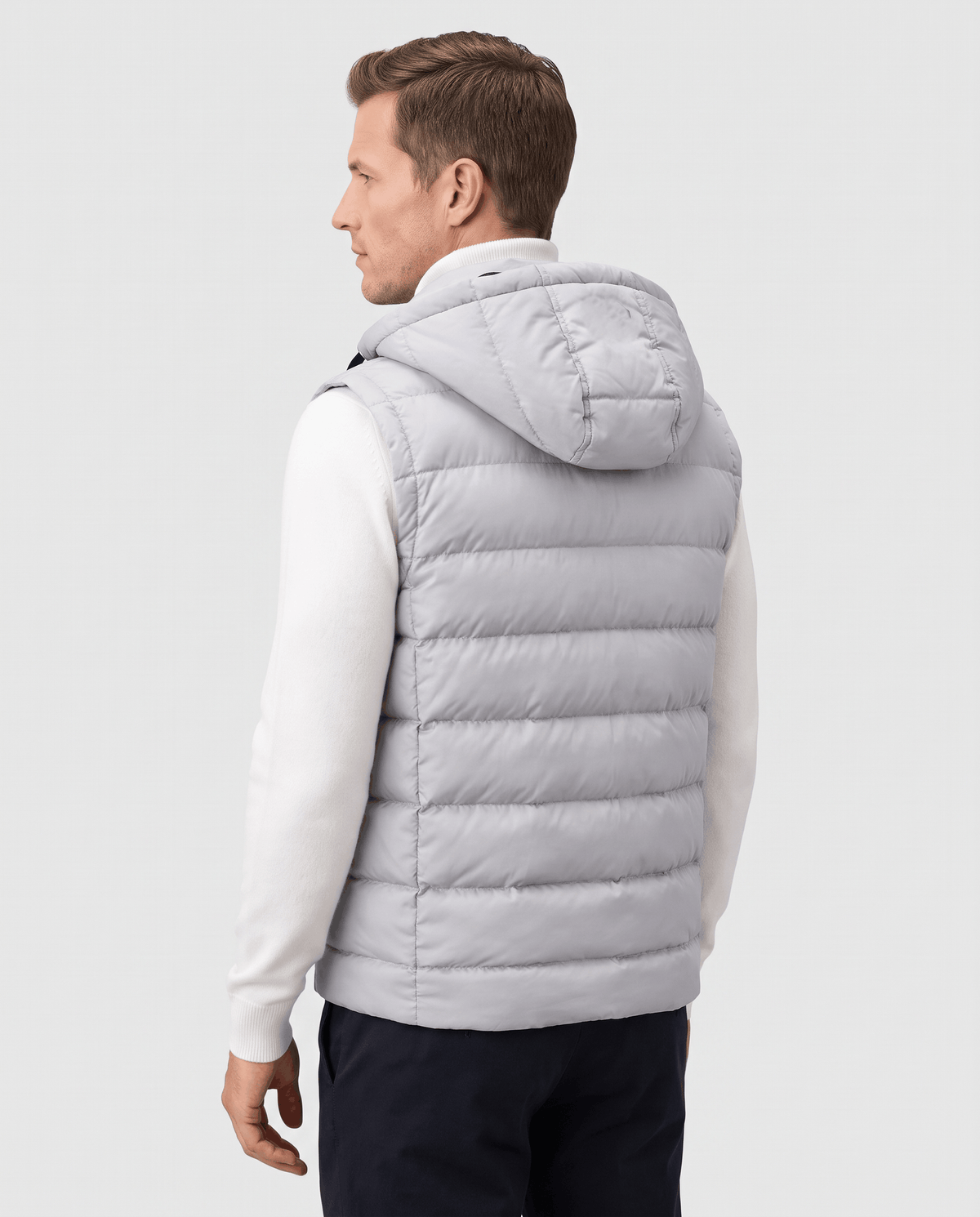 Back view of gray hooded quilted vest over a white sweater and dark trousers