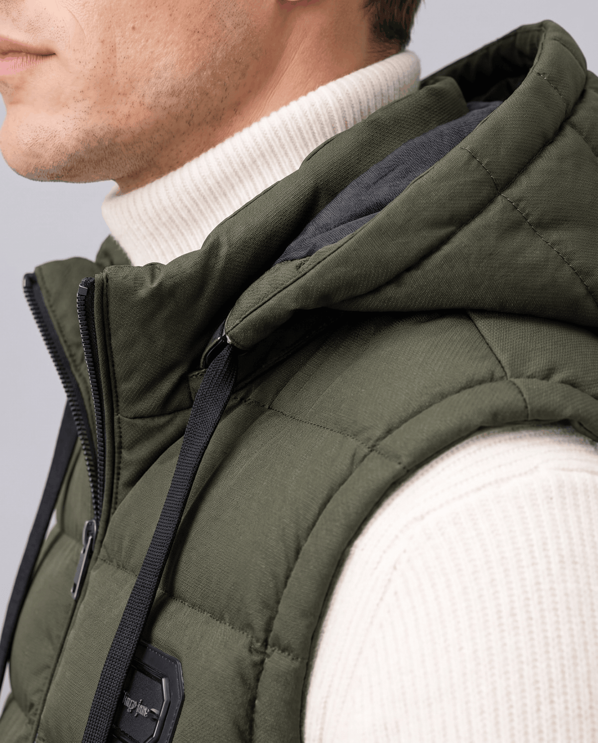 Side close-up of green vest showing the lined hood and high collar over a cream sweater