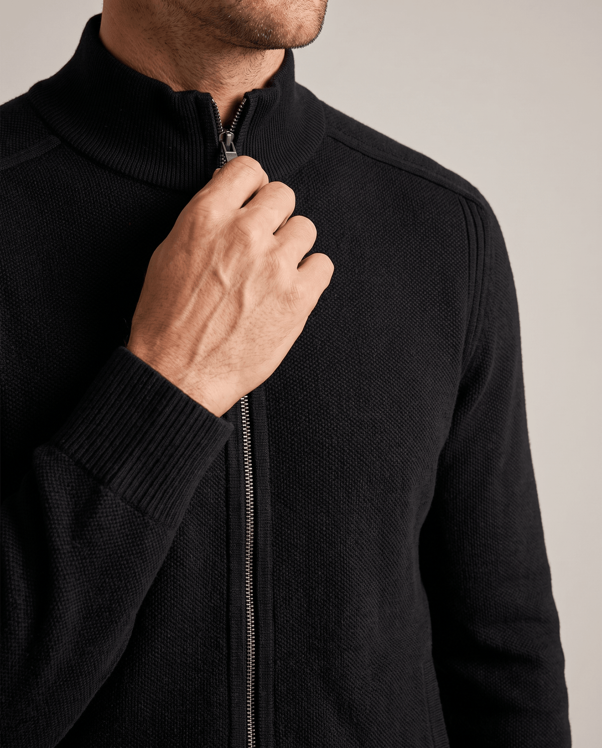 Close-up of a hand on the zip of the black knit cardigan