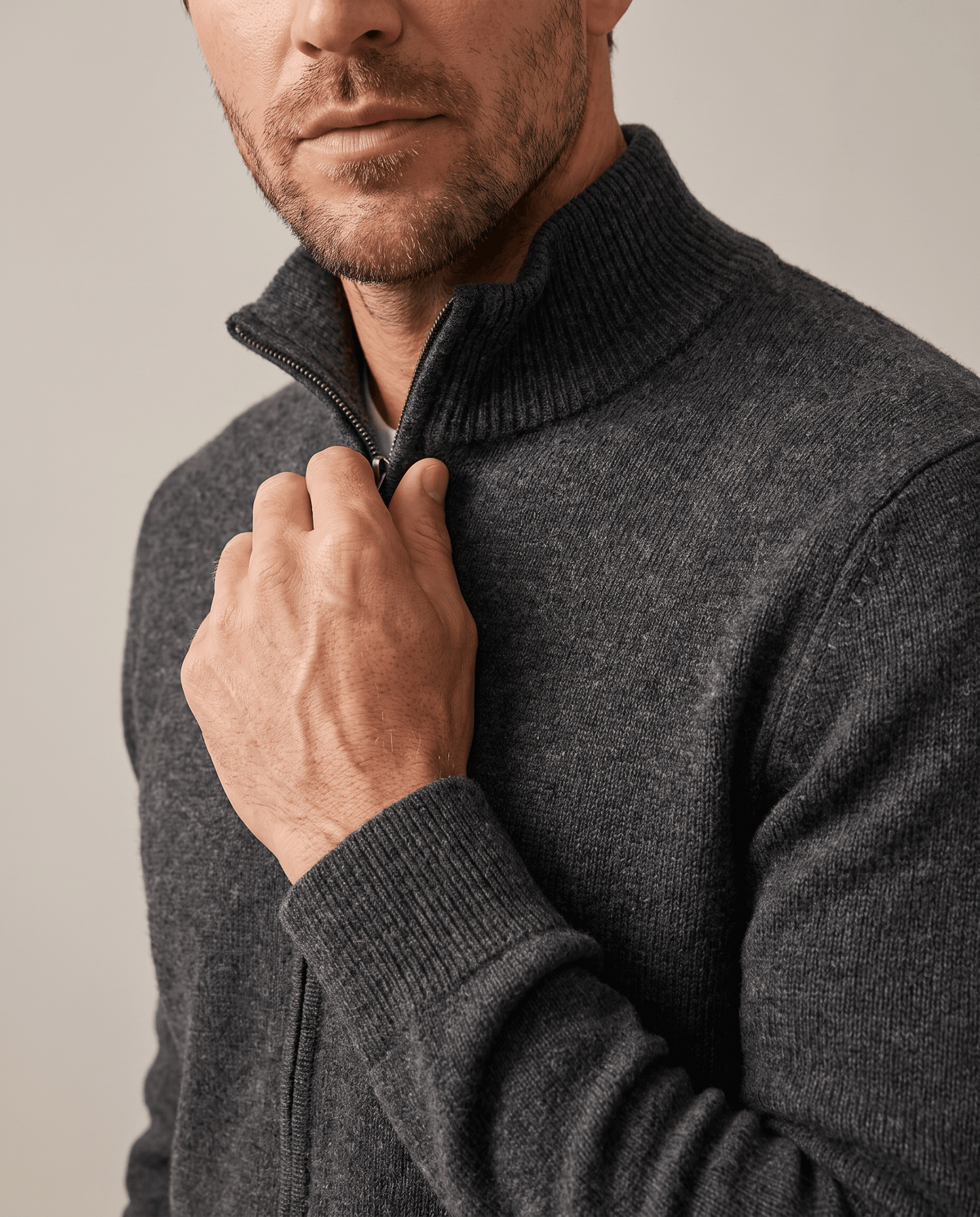 Hand adjusting the zip at the stand collar of a dark gray knit cardigan